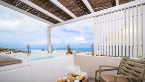 A balcony with a wooden bench, a tray with breakfast items, and a view of the sea and buildings. - Suite Home Santorini (Santorini)