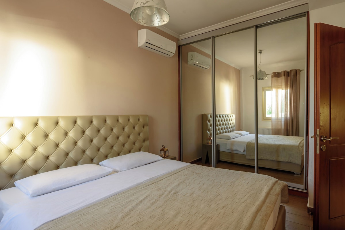 A bedroom with a tufted headboard, a bed with white linens, a nightstand with a lantern, and a sliding glass door leading to another room.