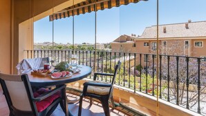 Un balcon avec une table dressée pour deux personnes, comprenant un verre d’eau, une assiette de pastèque et une petite plante.
