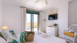 Une chambre à coucher avec un lit, un panier en osier, une commode blanche, une chaise en osier et un ventilateur de plafond.