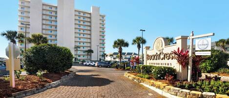 A beachfront condominium complex with a paved entrance, palm trees, and a sign for BeachCrest Condominiums.