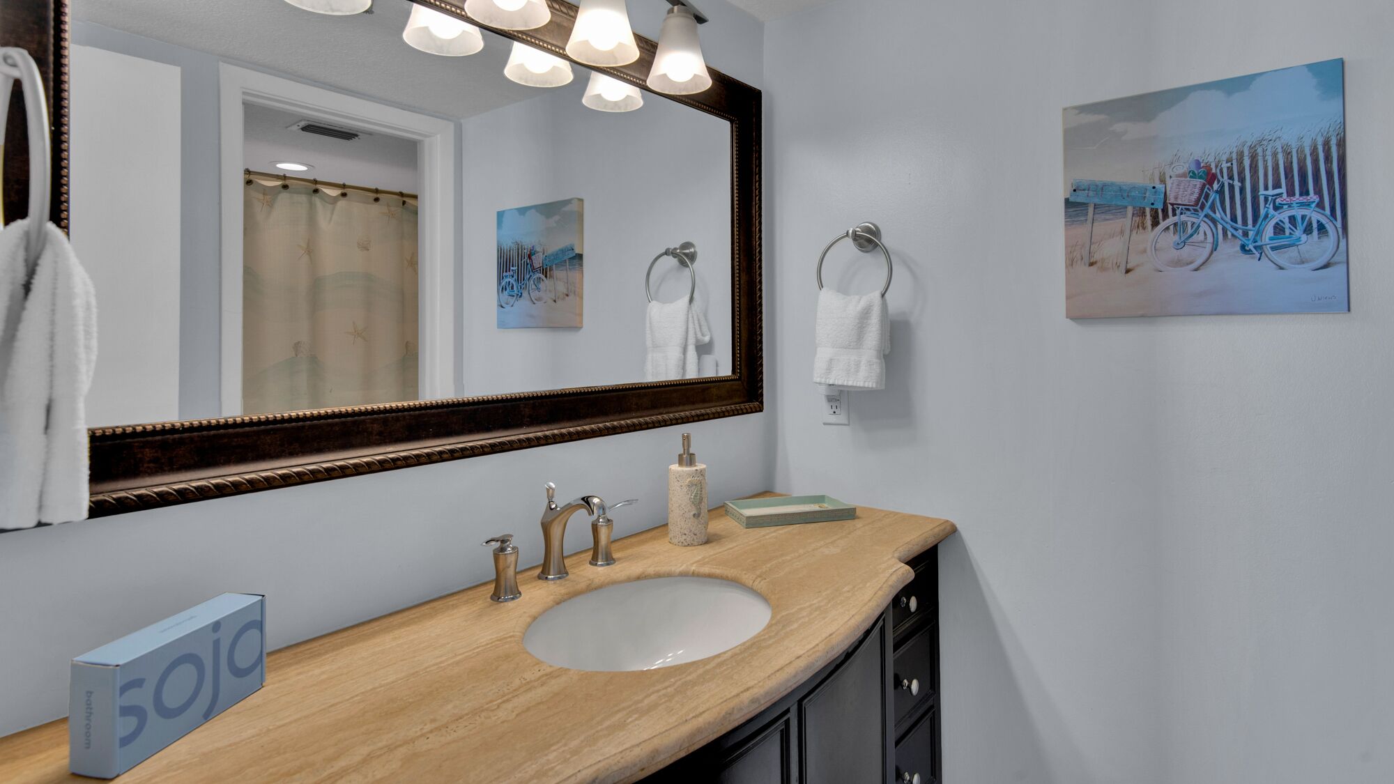 A bathroom with a wooden vanity, a large mirror, and a painting of a bicycle on the wall.