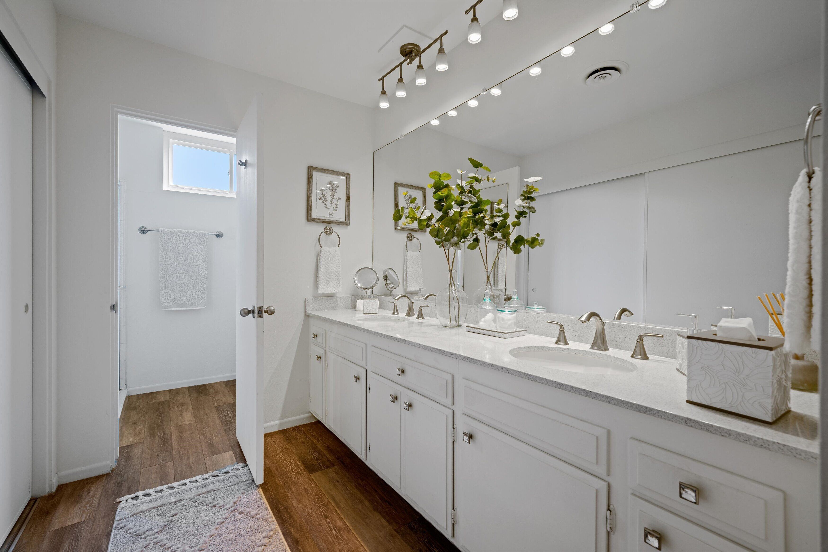 A modern bathroom with a large mirror, two sinks, and a window.