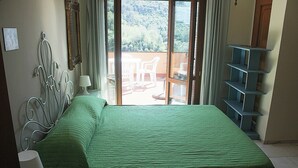 A room with a bed, a metal headboard, a window with curtains, and a view of a balcony with outdoor furniture. - Il Paradiso Vista Mare (Levanto)