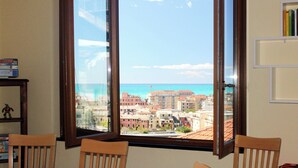A room with a large window offering a view of a coastal cityscape. - Il Paradiso Vista Mare (Levanto)