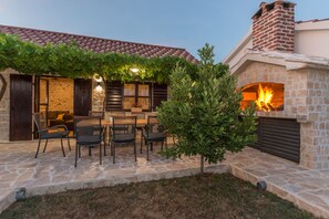 A stone patio with outdoor seating, a fire feature, and a covered area with a pergola. - Villa Vitis (Promina)