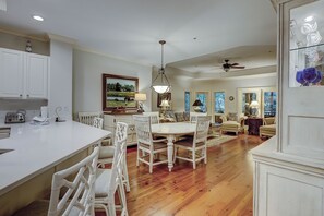 Una cocina amplia con muebles blancos, un comedor con sillas blancas, un ventilador de techo y un ventanal grande.