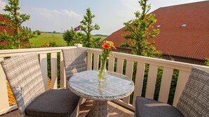 En balkon med fletmøbler, et glasbord og en vase med blomster.