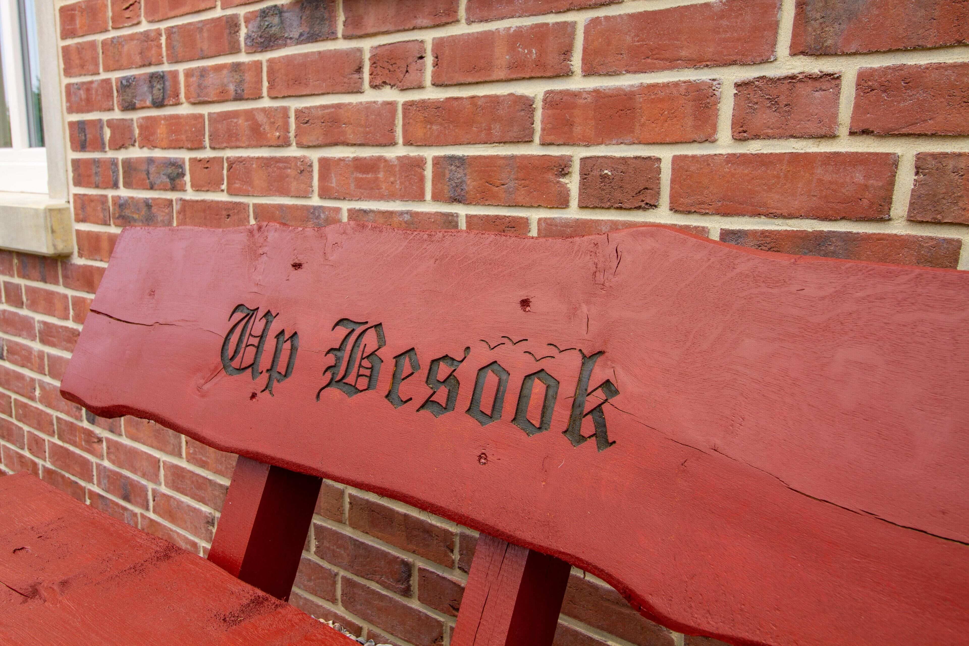 Un banc en bois sur lequel on peut lire l’inscription « Up Besook », adossé à un mur de briques.