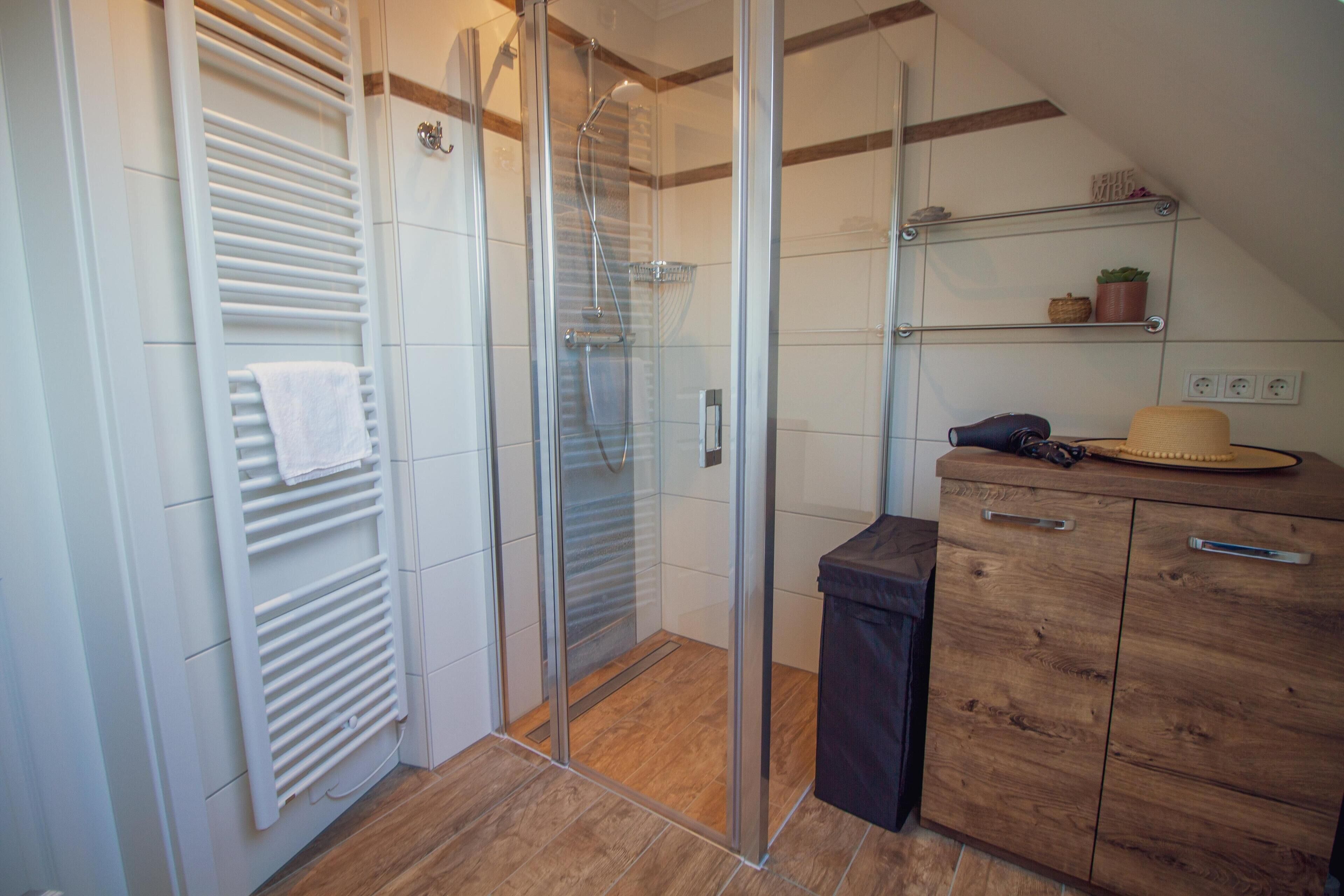 A modern bathroom with a glass shower enclosure, a wooden cabinet, and a towel rack.