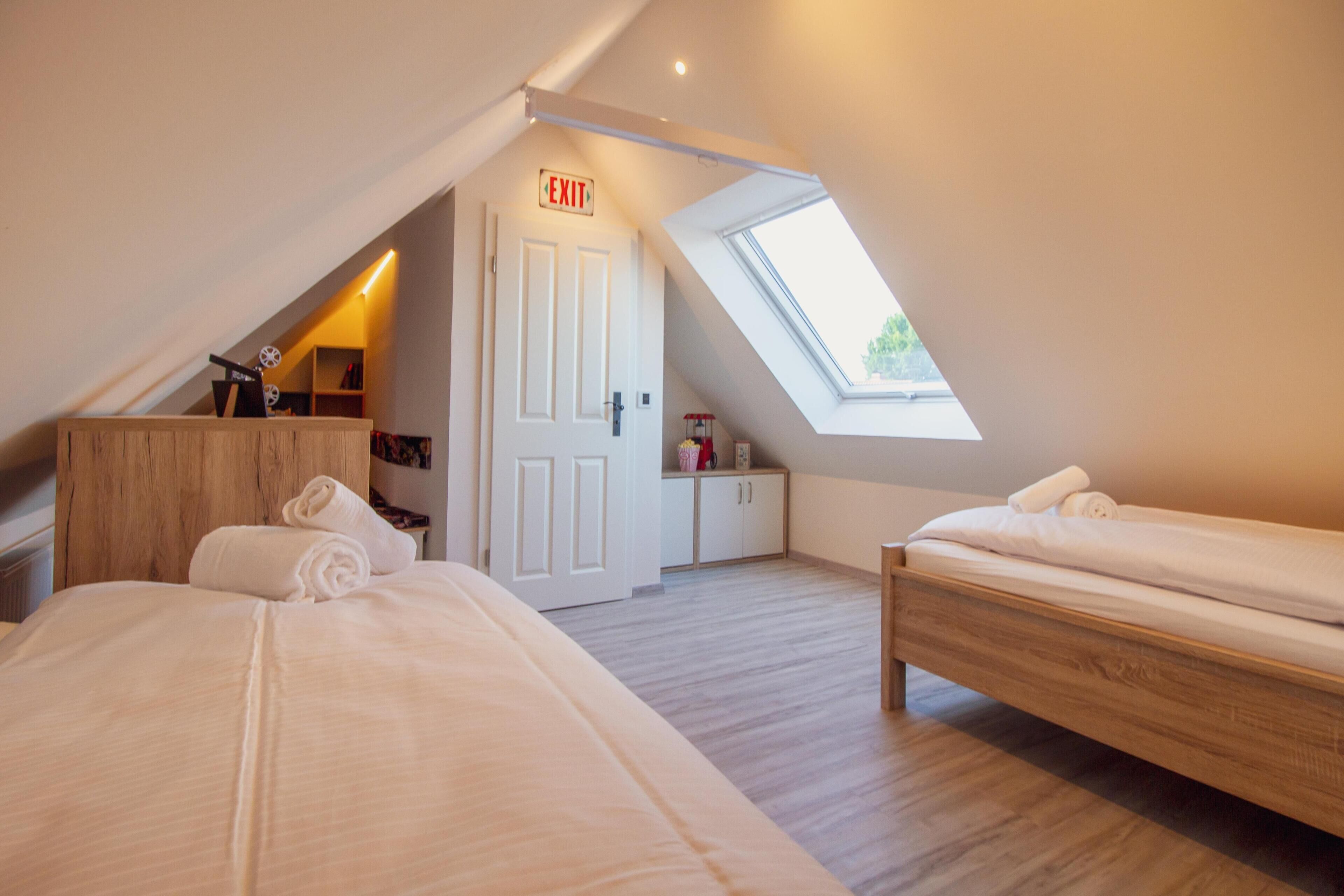 Een slaapkamer met twee bedden, dakraam, vluchtroute aanduiding en een kleine kitchenette.