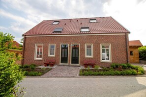 Een gebouw van baksteen met twee verdiepingen, een rode pannendak, een hoofdingang en twee ramen op de bovenverdieping.