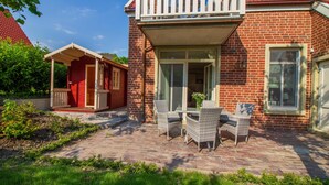 Une maison en briques rouges dotée d’un balcon, d’un porche abrité et d’une terrasse avec des meubles en osier.
