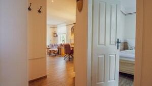 Une chambre d’hôtel avec un plancher en bois, un lit avec une literie blanche et une porte donnant sur un coin repas équipé d’une table et de chaises.