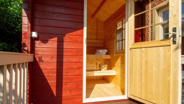 Une cabane en bois à l’extérieur rouge, avec une porte en bois et une petite fenêtre.