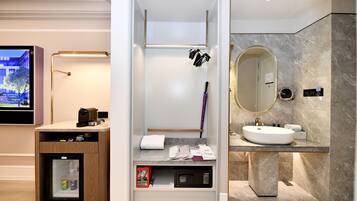 A modern bathroom with a vanity, a shower area, a built-in refrigerator, and a television.