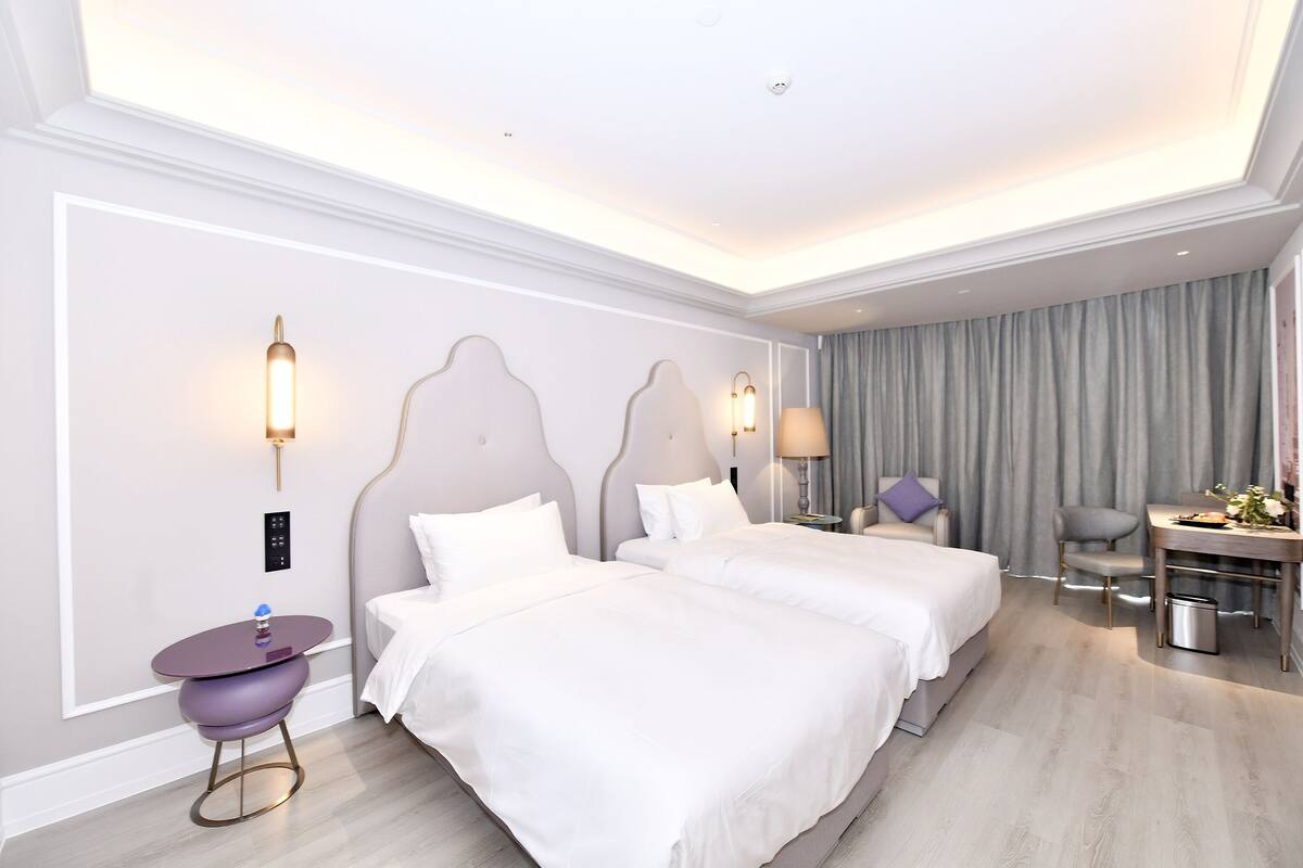 Ein Hotelzimmer mit zwei Betten, einem Schreibtisch, einem Stuhl und einem kleinen Tisch.