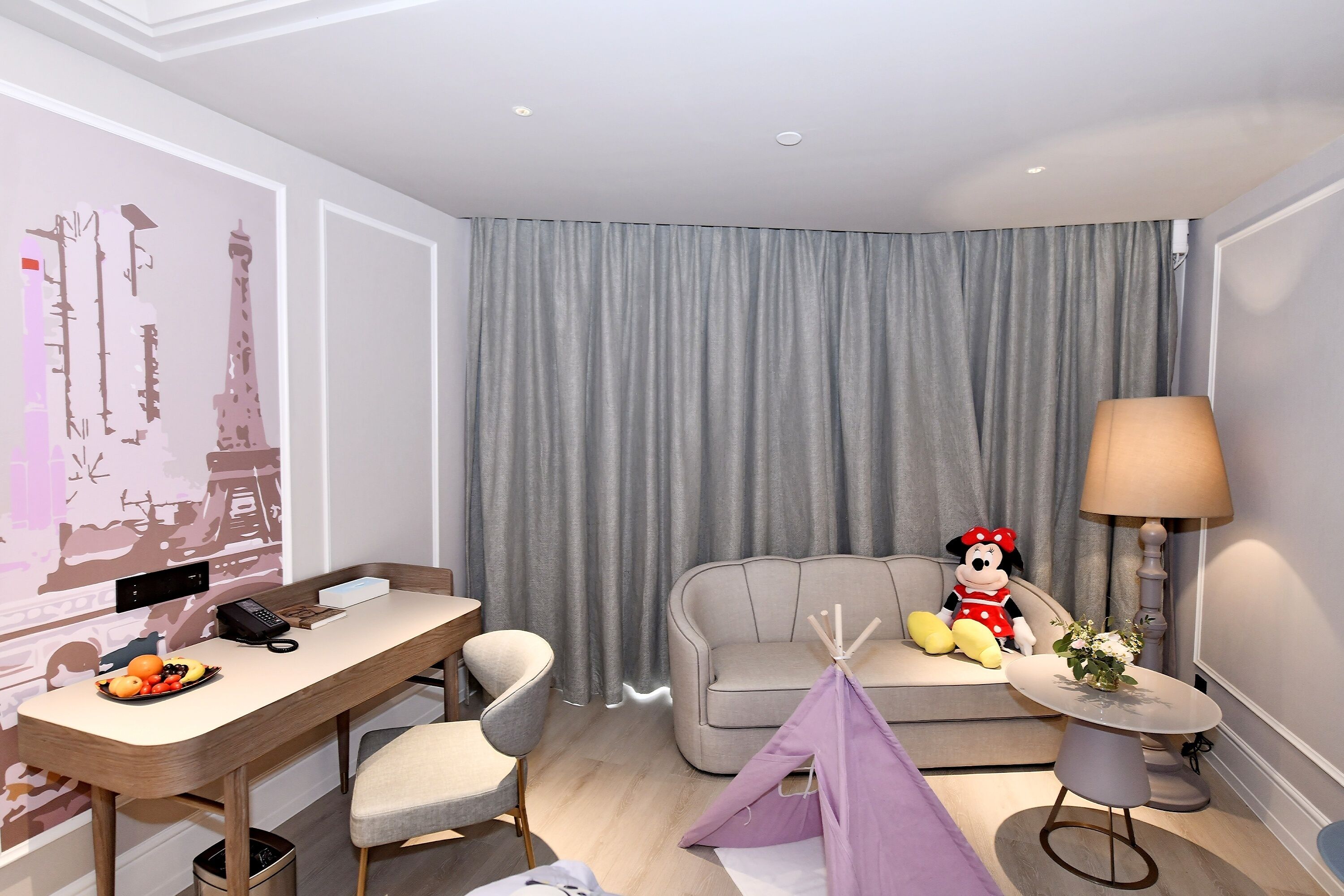 Habitació d'hotel moderna amb escriptori, sofà, làmpada, joguina tova i una tenda.
