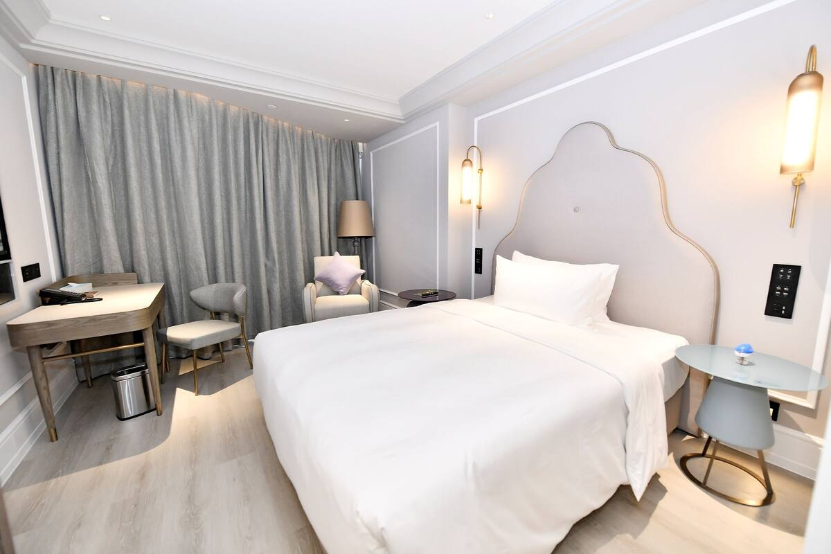 Ein Hotelzimmer mit einem großen Bett, einem Schreibtisch, einem Stuhl, einem kleinen Tisch und einer Lampe.