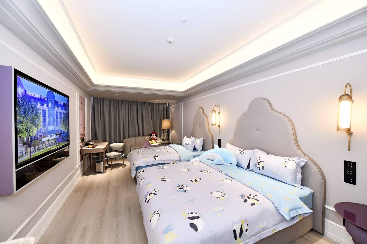Ein Hotelzimmer mit einem großen Fernseher, zwei Betten mit Panda-Muster-Bettwäsche, einem Schreibtisch mit Stuhl und einer Essecke mit Tisch und Stühlen.