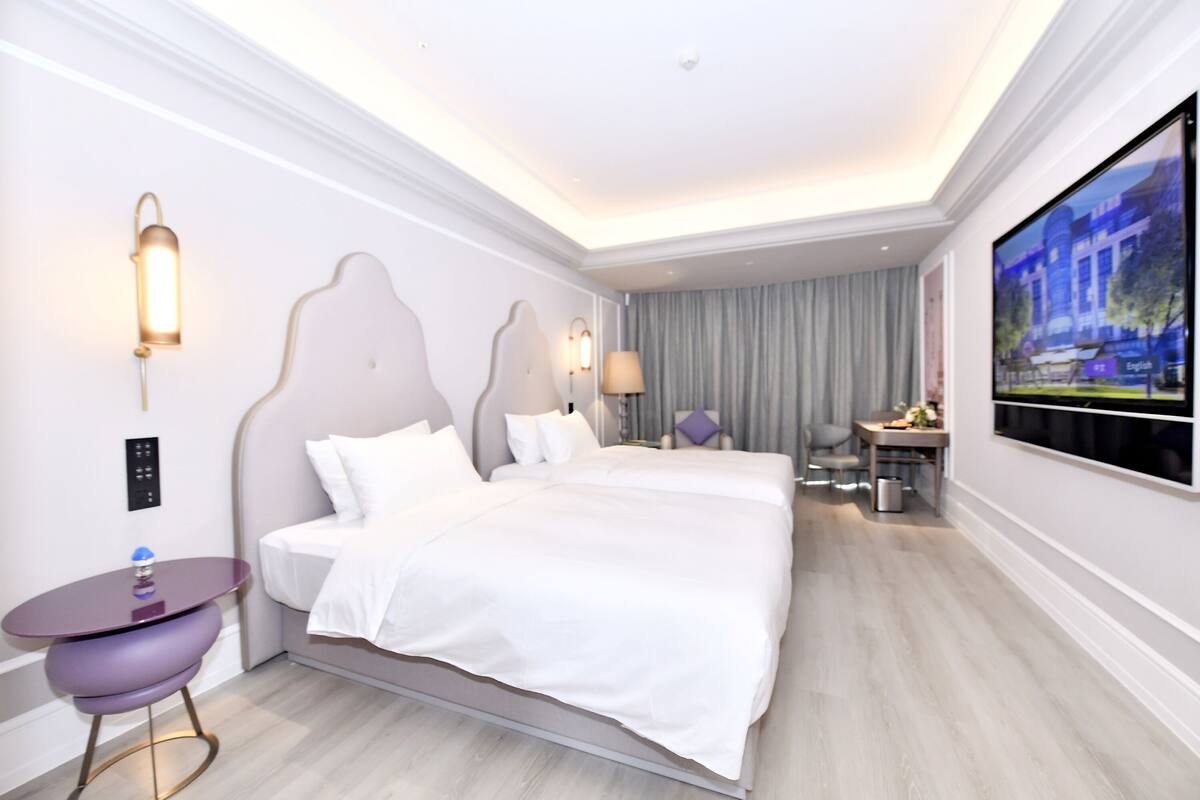 Ein modernes Hotelzimmer mit einem großen Bett, einem Schreibtisch, einem Sessel, einem Fernseher und einer Wandleuchte.