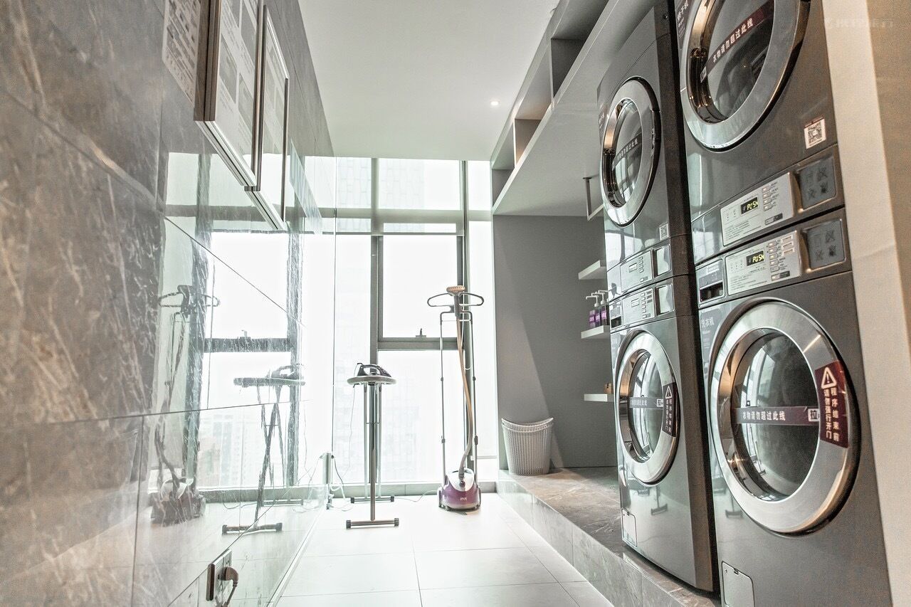 A modern laundry room with a glass wall, a vacuum cleaner, and stacked washing machines.