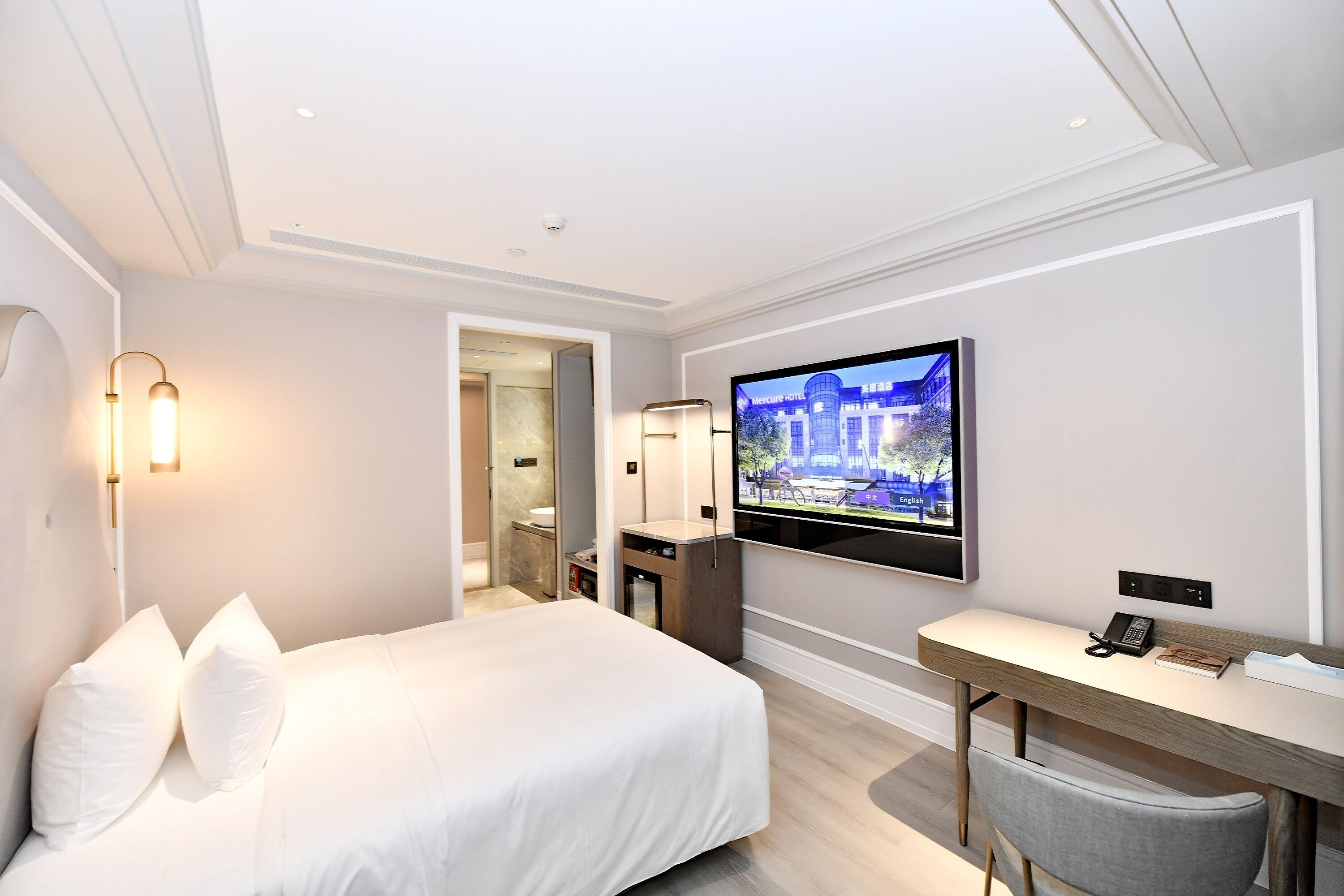 Une chambre d’hôtel avec un lit, un bureau, une télévision et une salle de bain visible à travers une porte ouverte.