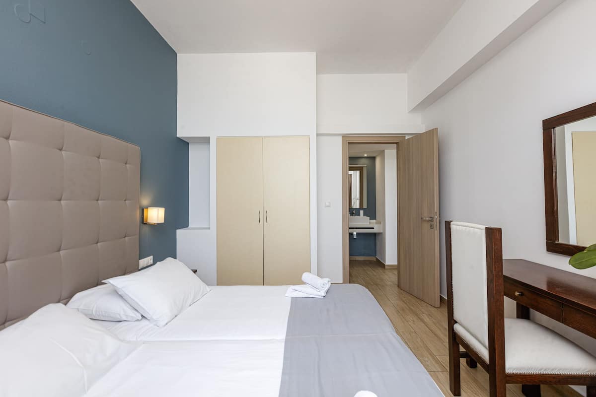 A hotel room with a large bed, a bedside table, a chair, and a bathroom visible through an open door.
