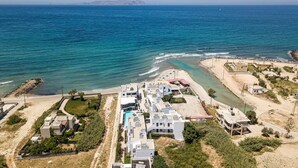An aerial view of a coastal residential area with modern buildings, a swimming pool, and a beach.