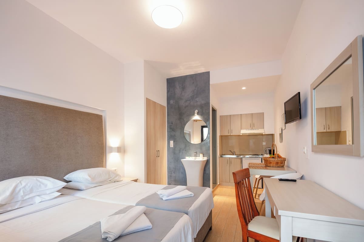 A hotel room with two beds, a desk, a chair, a sink, and a television.