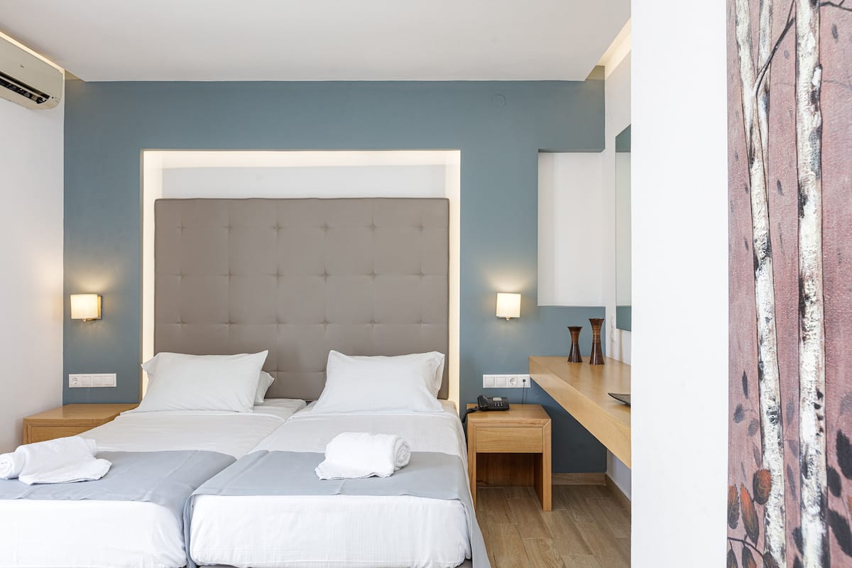 A hotel room with two beds, a large headboard, bedside tables, a nightstand, a mirror, and a wall with a textured pattern.