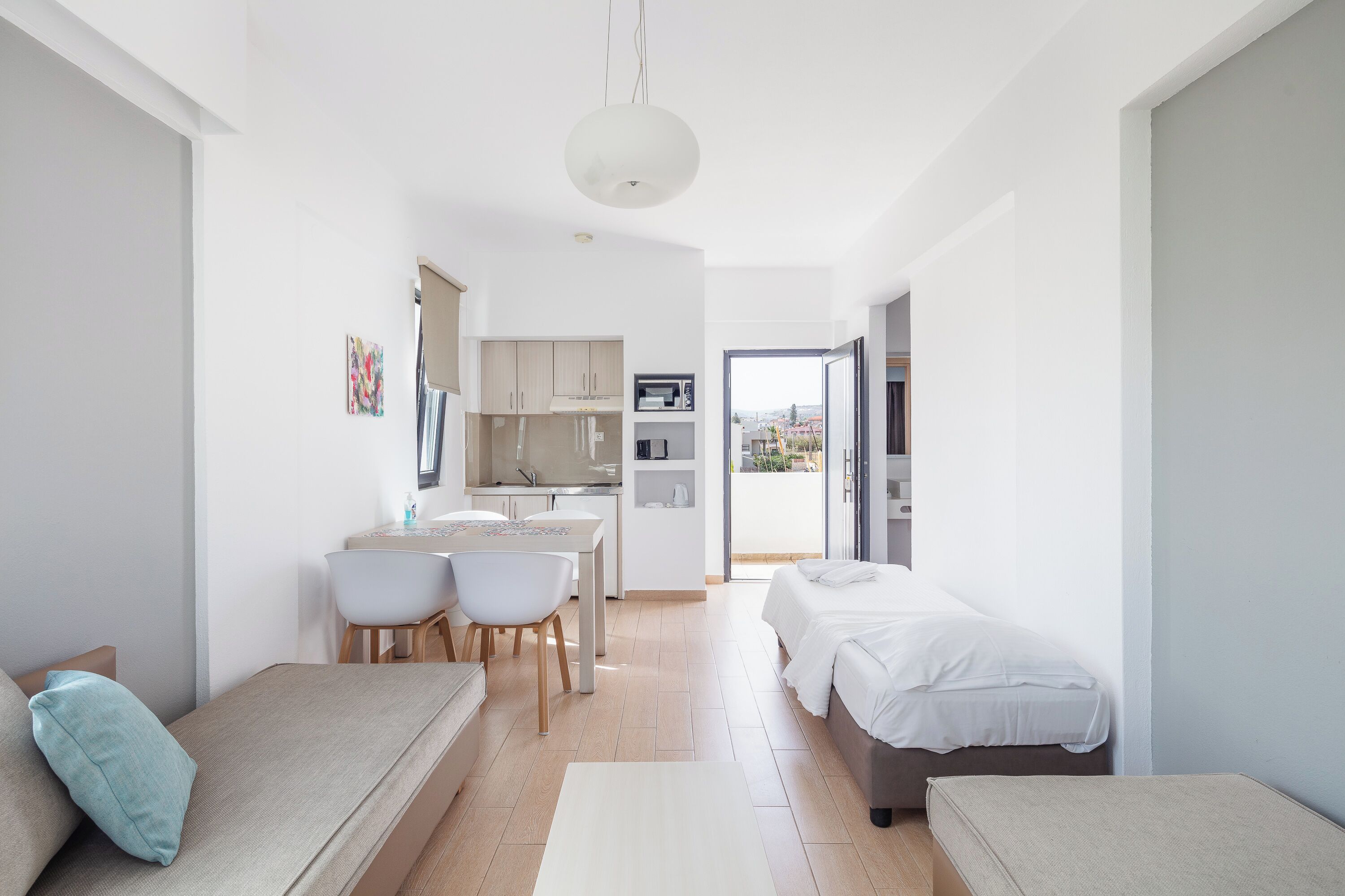 A modern, compact living space with a kitchenette, a dining area, and a bedroom with a balcony.