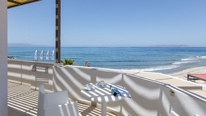 A balcony with a table and chairs, overlooking a beach and the sea.
