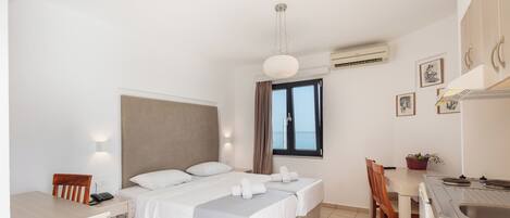 A hotel room with a bed, a desk, a chair, a small table, a window with curtains, and a sink.