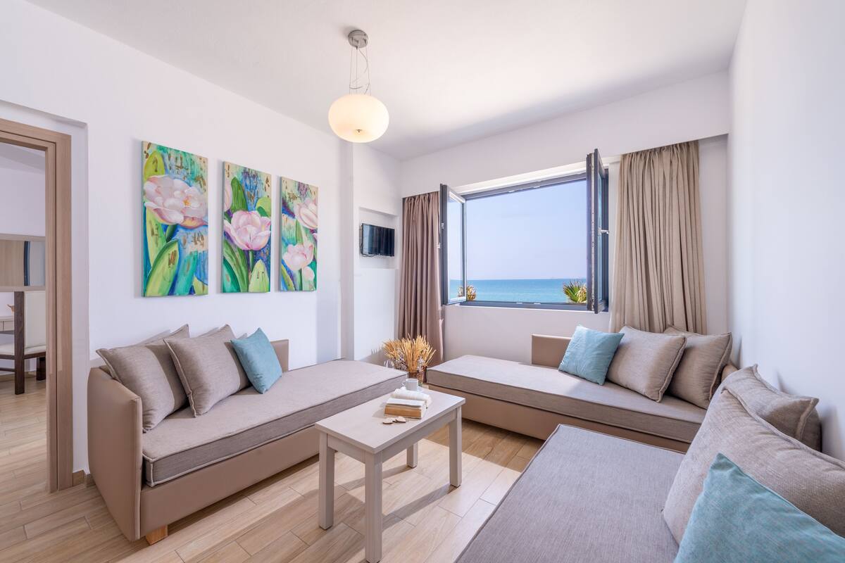 A modern living room with a sofa set, a coffee table, and a large window with a view of the sea.