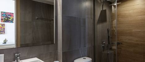 A modern bathroom with a large mirror, a white sink, a glass-enclosed shower, and a wooden wall.