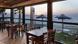 A restaurant with wooden tables and chairs, large windows overlooking the sea, and a sign reading "Find your spot."