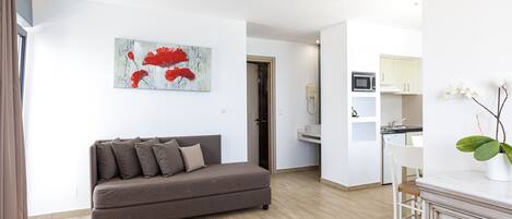 Een moderne woonkamer met een bruine bank, een witte salontafel en een keuken met witte kastjes en een magnetron.