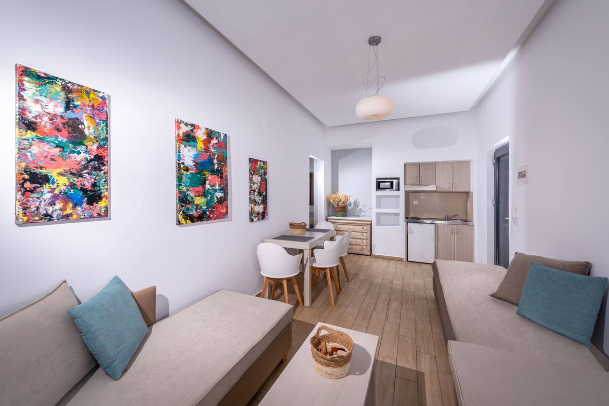 A modern living room with a sofa, a dining table with chairs, and a kitchen area with cabinets and a microwave.