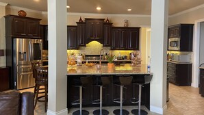A modern kitchen with dark wood cabinets, stainless steel appliances, and a central island with bar stools. - Lakefront Property -Small Gatherings  (Houston)