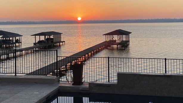 A waterfront with a pier extending into calm water, featuring several covered seating areas and a clear view of the sunset. - Lakefront Property -Small Gatherings  (Houston)