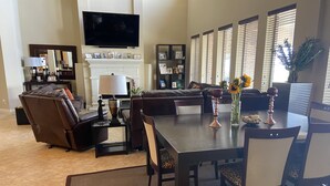 A modern living room with a fireplace, a flat-screen TV, a dining area with a table and chairs, and a sofa. - Lakefront Property -Small Gatherings  (Houston)