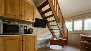 Una cocina con armarios de madera, microondas, cafetera, televisor montado en la pared y una escalera de madera.