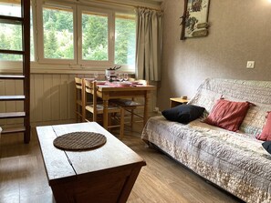 A cozy room with a wooden dining table set for two, a sofa with patterned upholstery, and a window with curtains.