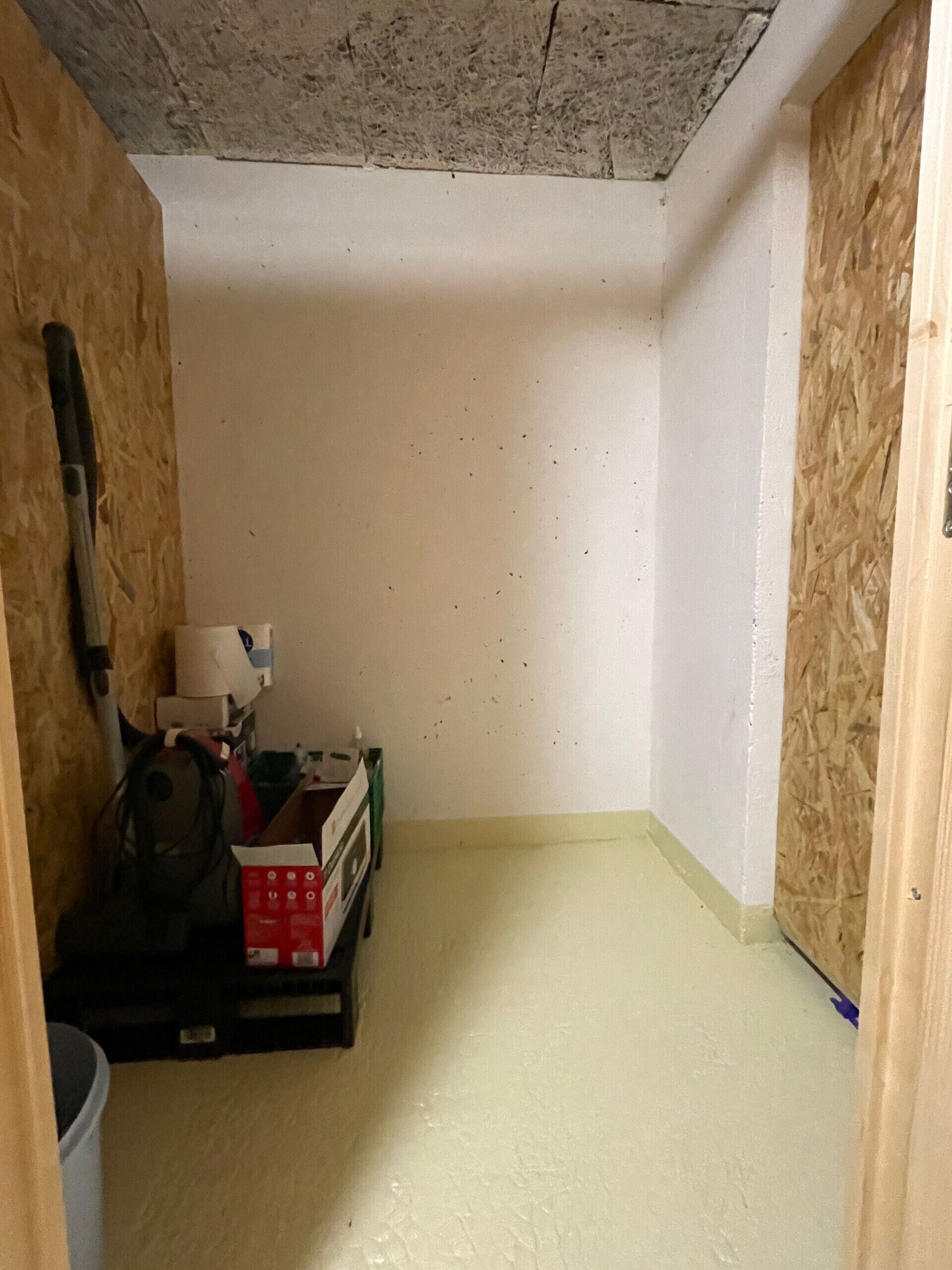 Una habitación pequeña, sin terminar, con techo y paredes a la vista, un aspirador y una caja de herramientas.
