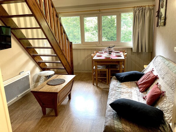 A cozy room with a wooden staircase, a dining table set with plates and glasses, a sofa with cushions, and a window with curtains.