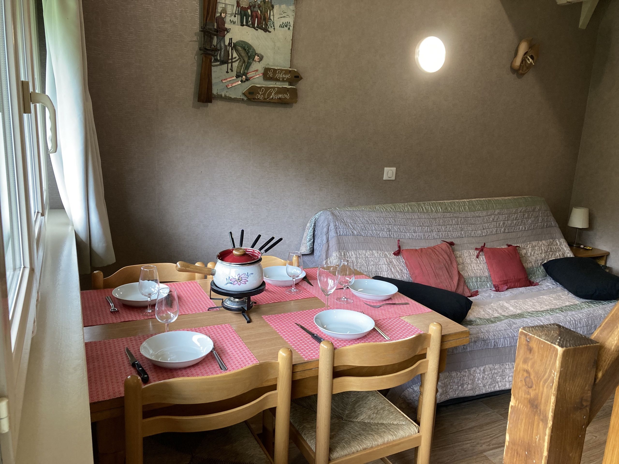 A dining area with a table set for two, a painting on the wall, and a sofa with cushions.