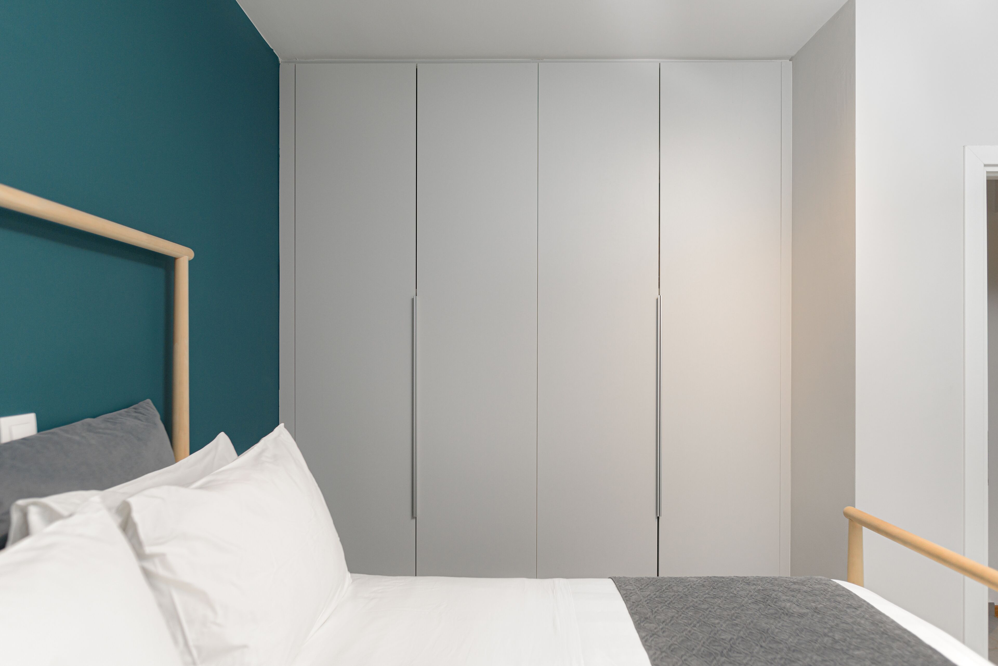 Un dormitorio con cama, cabecera de madera, pared de acento color aguamarina y armario gris.