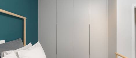 Un dormitorio con cama, cabecera de madera, pared de acento color aguamarina y armario gris.