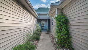 A narrow pathway flanked by two beige houses with a small garden area and a blue door visible in the background. - TB 94B Dog friendly Garden home in the peaceful True Blue community. (Pawleys island)